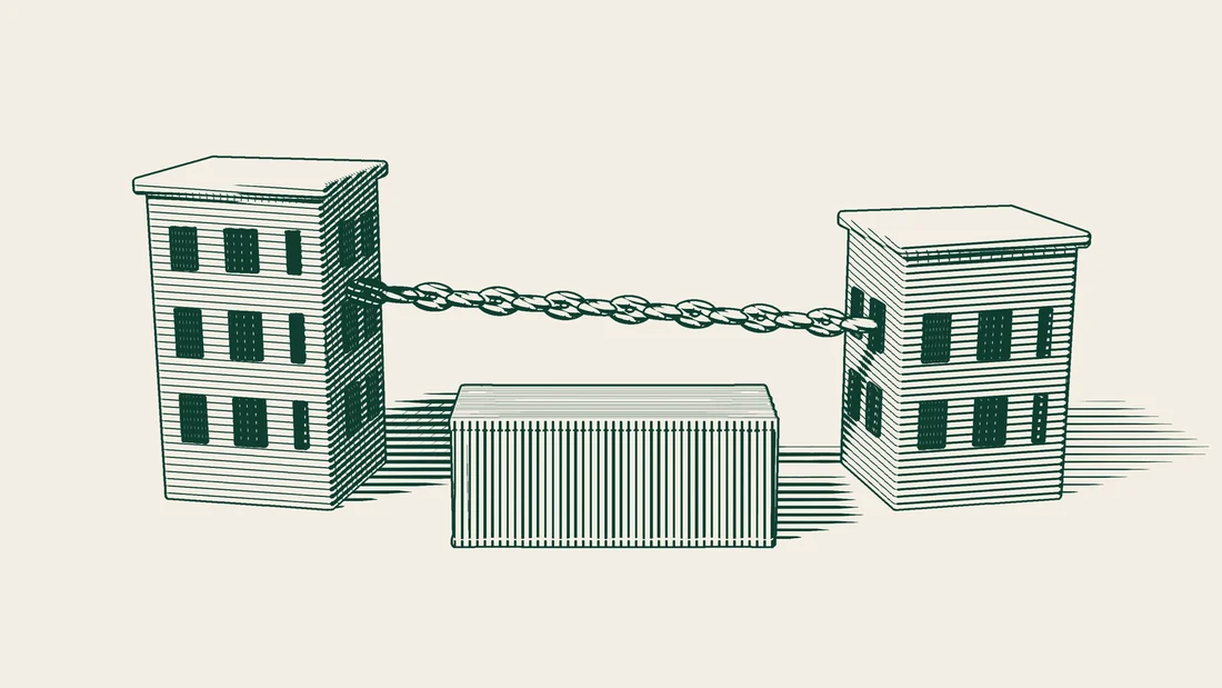 The buildings of an importer and a customs broker linked by a chain that runs over a shipping container.