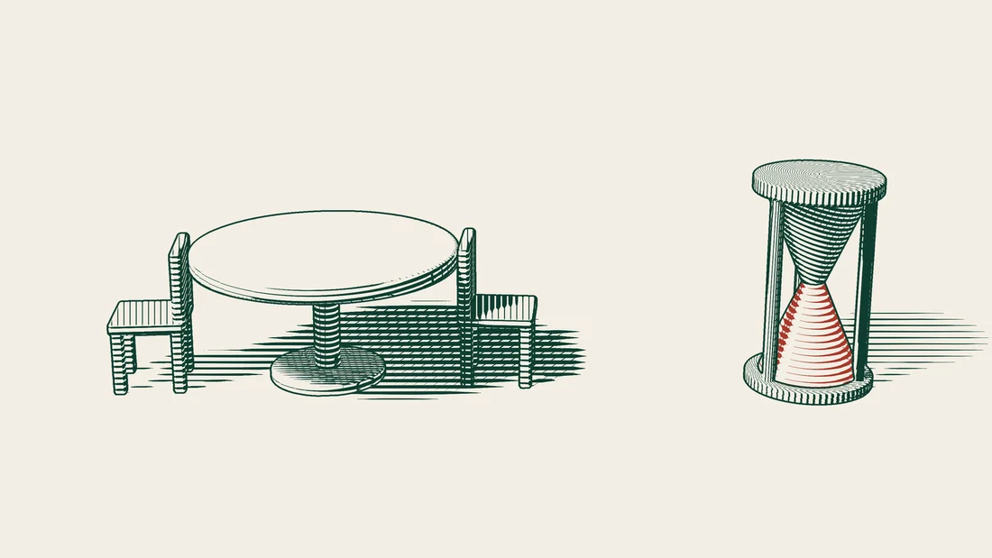 An hourglass stands beside a table set with two chairs facing each other.