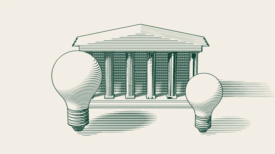 Two light bulbs, one large and one small, stand in front of the same columned institutional building.