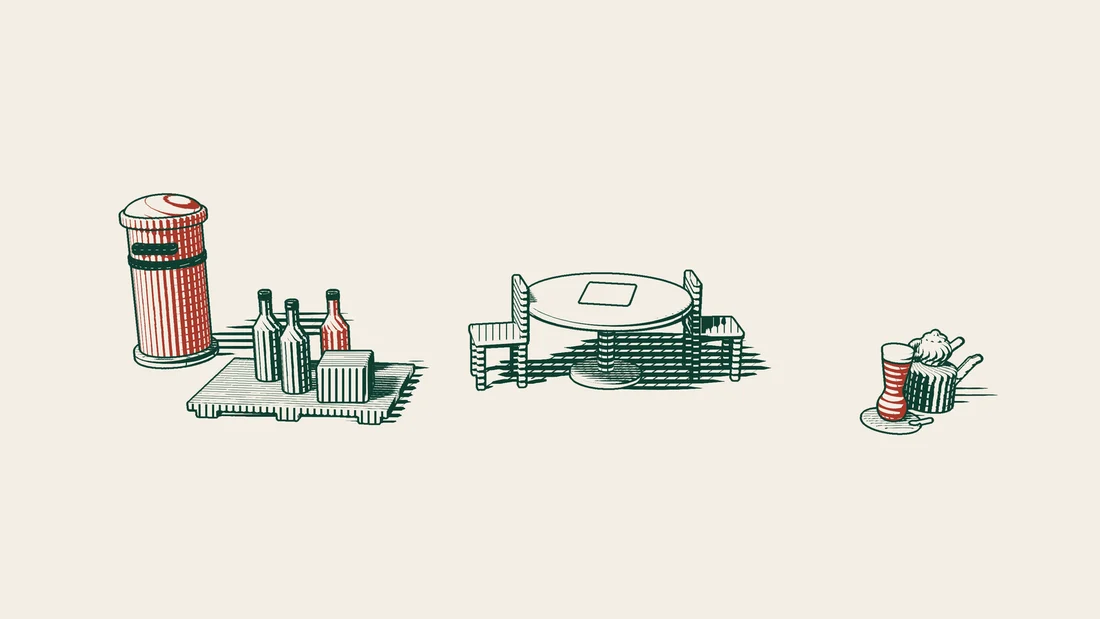Unlabelled bottles on a pallet beside a table with two empty chairs face to face, a red postbox on one side and a Turkish tea set on the other.