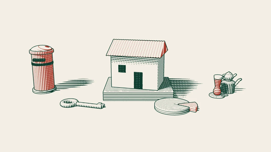 A tiled-roof house on a stone plinth with a brass key and a sliced disc in front, a distant red postbox and a Turkish tea set beside it.