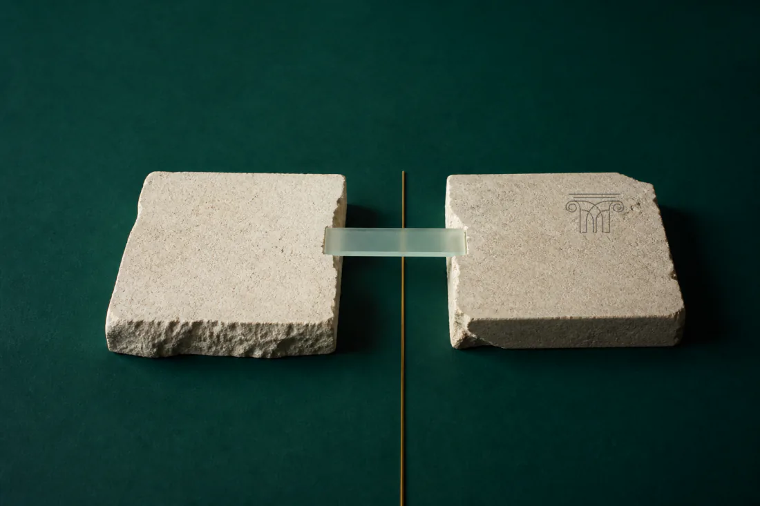 Two rough limestone blocks set apart, bridged by a single pane of frosted glass; a thin brass line marks the gap between them